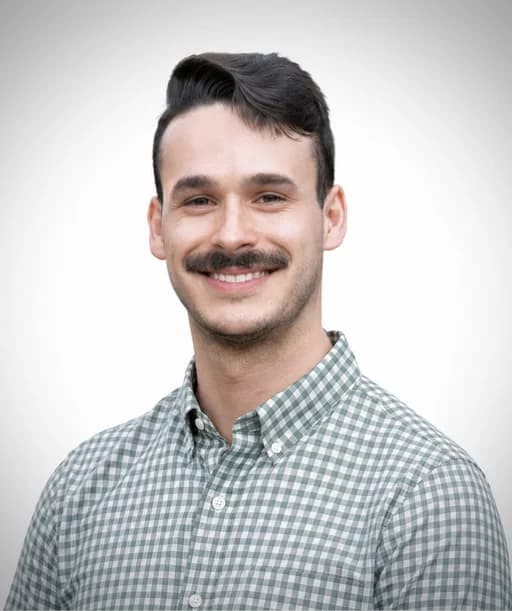 Enzo Plaitano, a man with a moustache wearing a blue gingham shirt, photographed against a plain grey studio backdrop